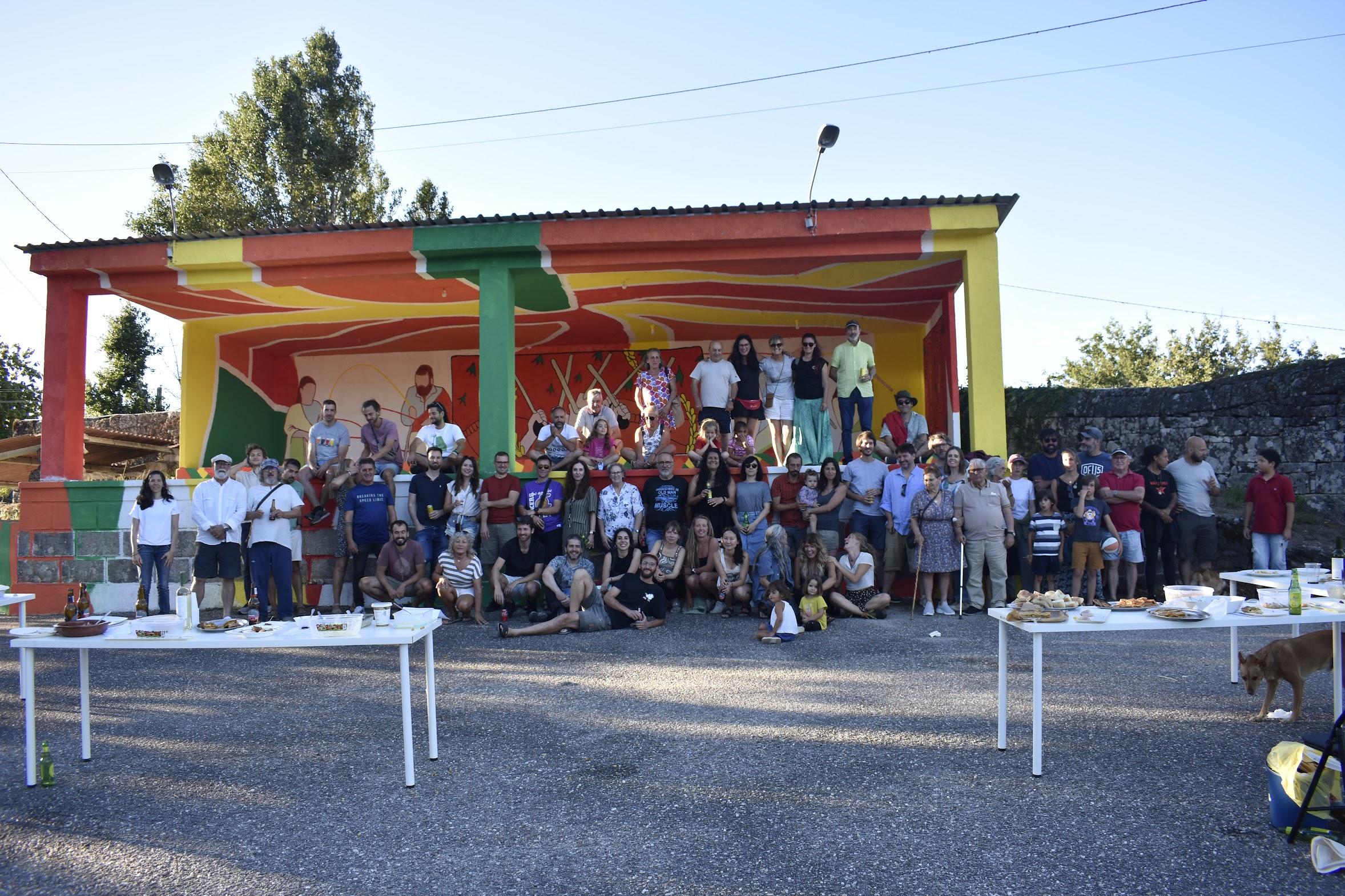 Veciñanza reunida diante dun escenario cun mural de cores